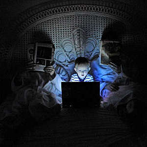 A little boy stares at a laptop screen while his parents are reading.