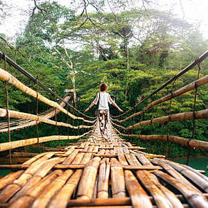 Back view of young woman on suspension wooden bamboo bridge across Loboc river in Bohol, Philippines