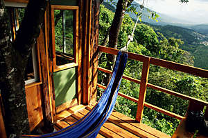 Relaxing scene with a hammock on the balcony of a treehouse offering a beautiful view over a tropical valley.