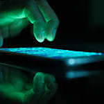 Hacker’s hand working on a smartphone reflects blue underglow from the screen