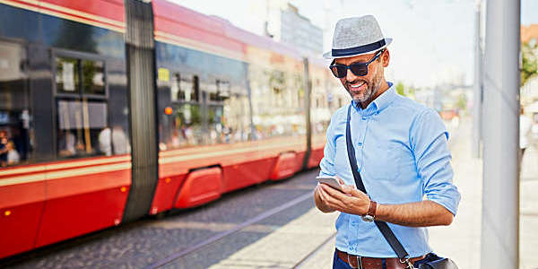 Tourist checks tram schedule on his smartphone as a red tram pulls up.