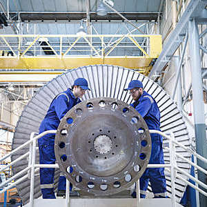 Two engineers in blue caps and overalls repair a steam turbine in a workshop.