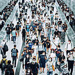 Stream of commuters with protective face masks during rush hour at a busy subway station.